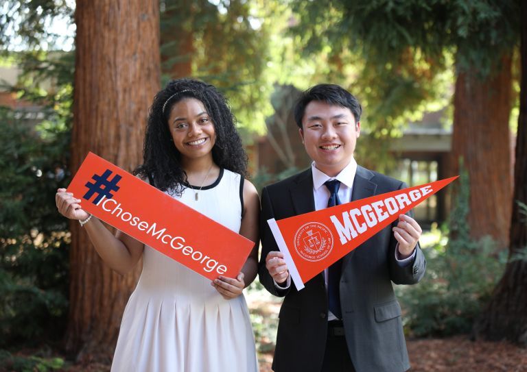two students holding signs. left: I Choose McGeorge, right: McGeorge